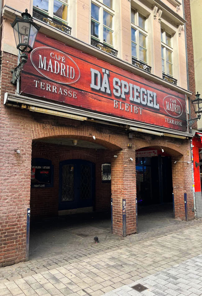 Backsteinfassade eines Restaurants mit roter Leuchtschrift und Terrasse
