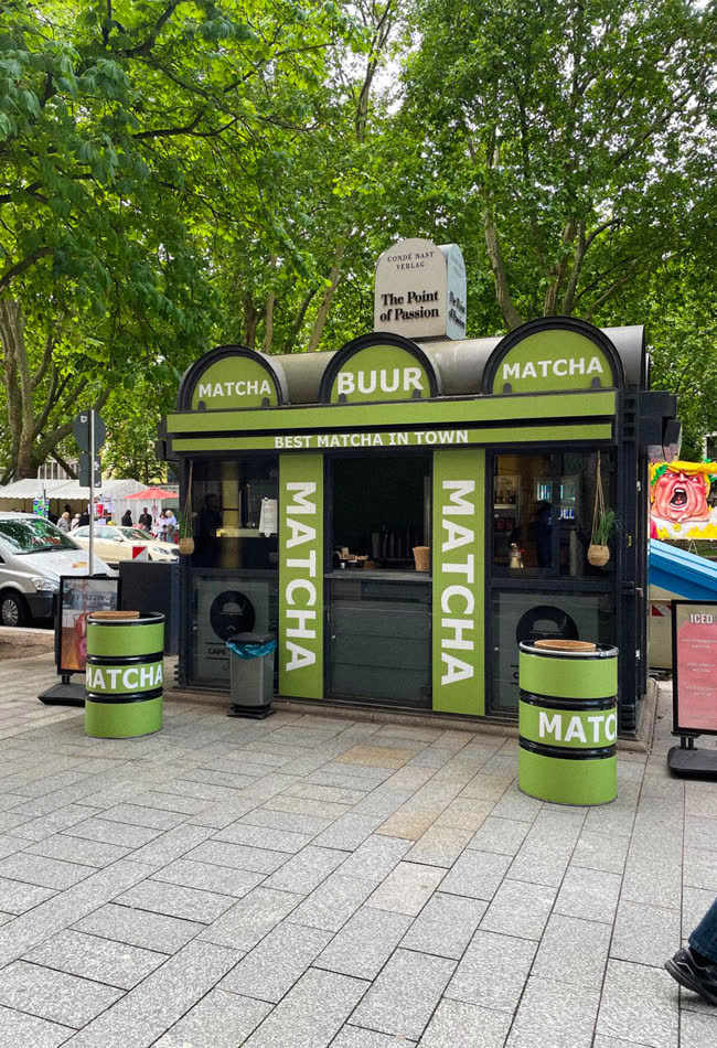 Grüner Kiosk mit Matcha-Schriftzügen auf einem Platz